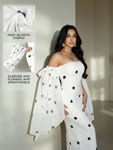 A woman models a white off-the-shoulder maxi dress with black polka dots and flowing sheer sleeves. The image includes an inset showing close-ups of the high-elastic fabric and flowing sleeve material with text overlays.
