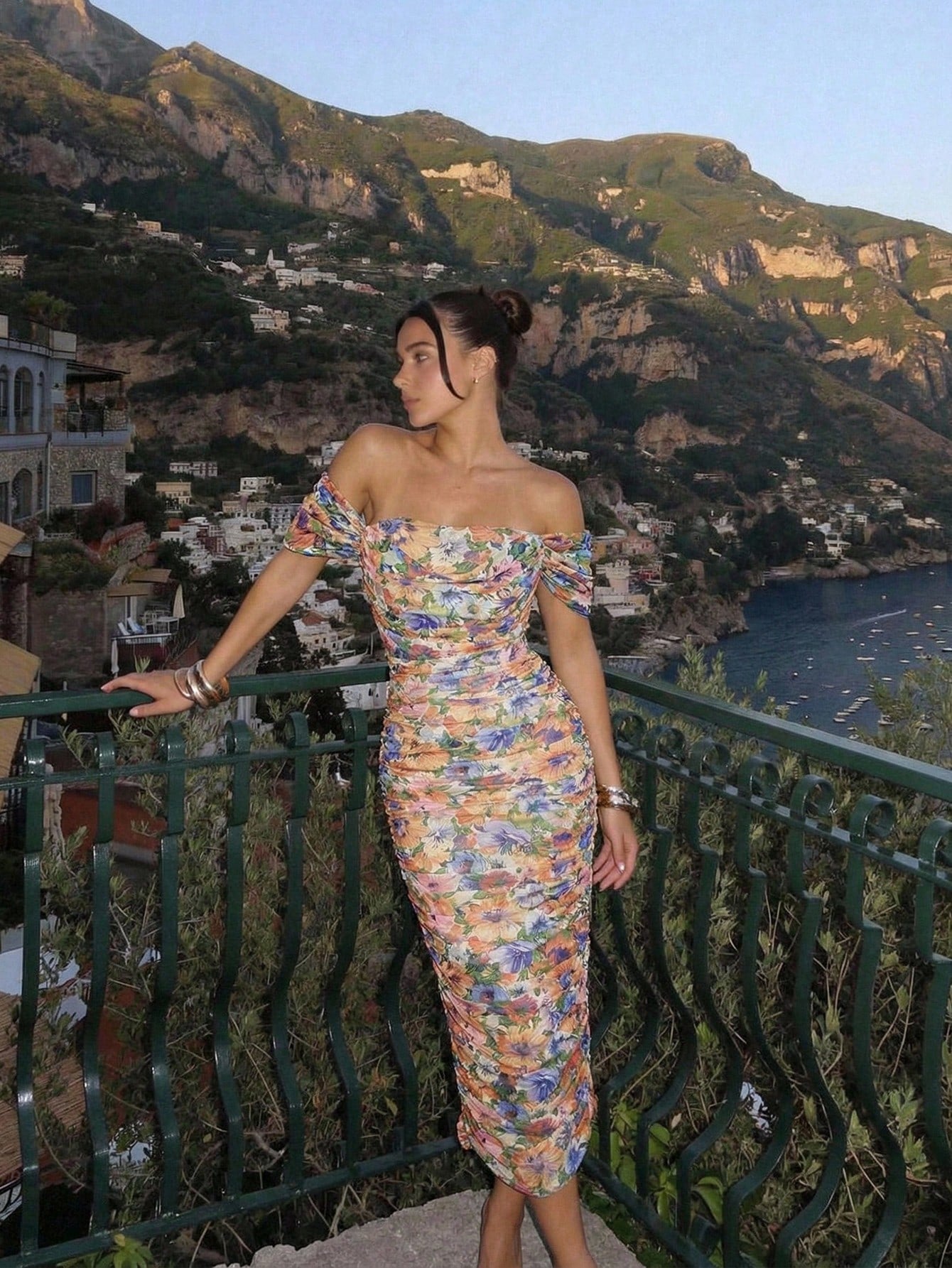 Woman in a floral dress standing on a balcony with a scenic mountain view.