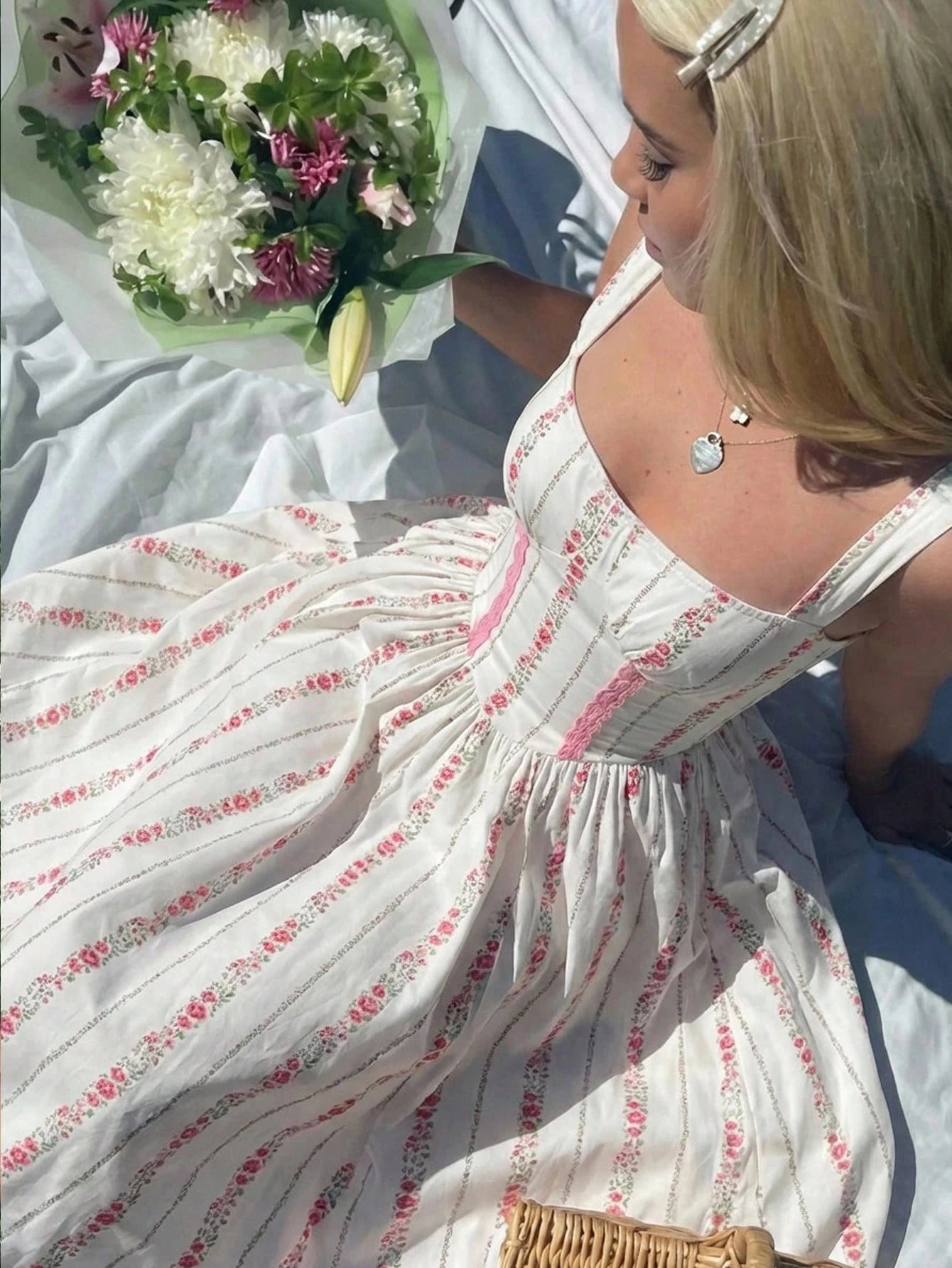 Woman in a floral dress holding flowers, lying on a white blanket.
