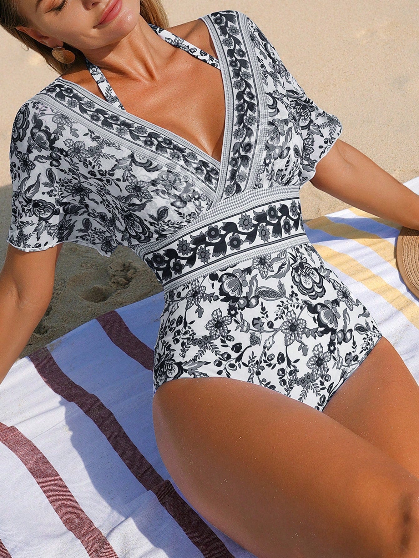 Woman wearing a black and white floral swimsuit on a beach.
