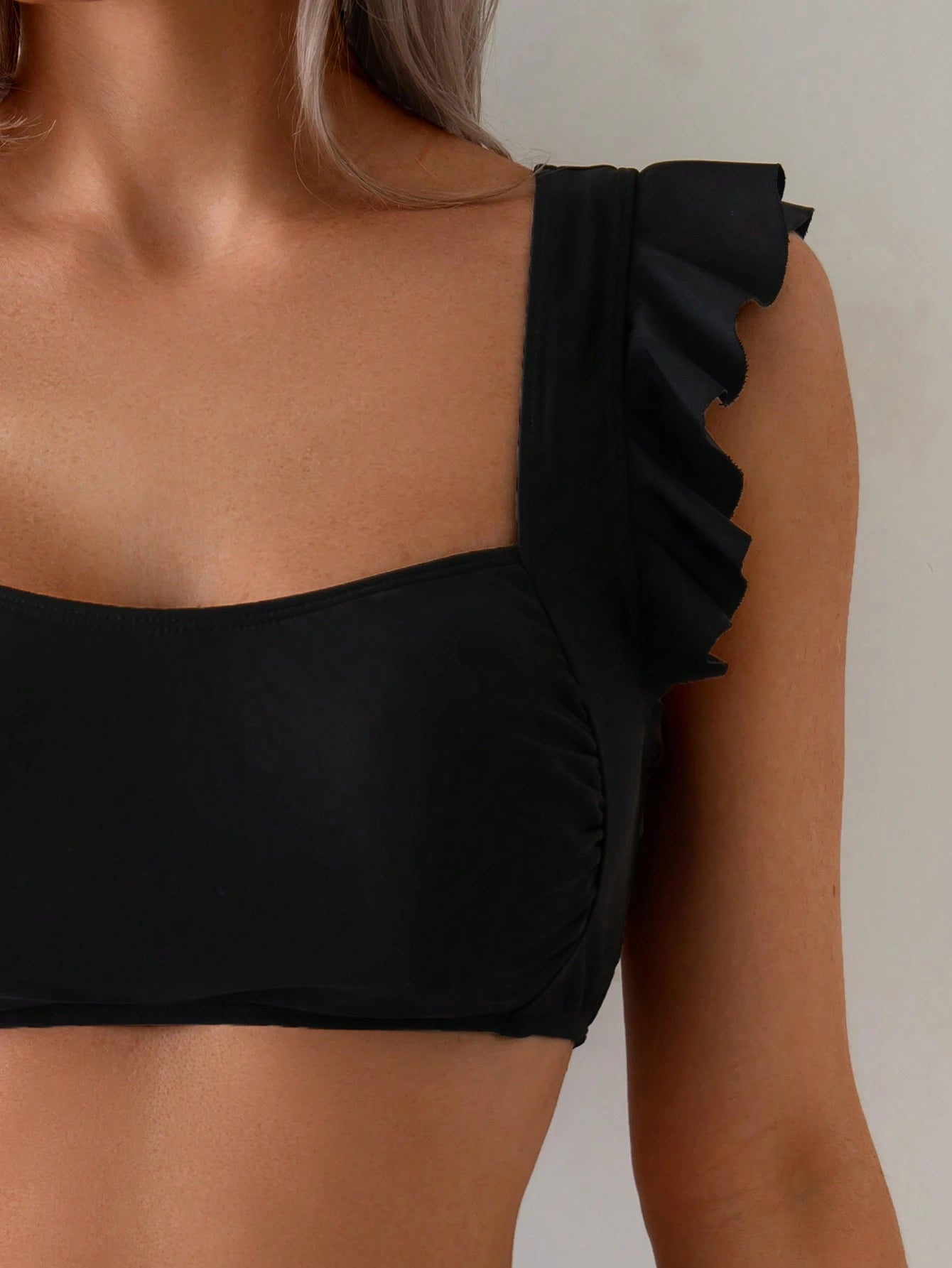 Black one-shoulder top with ruffled details on a neutral background