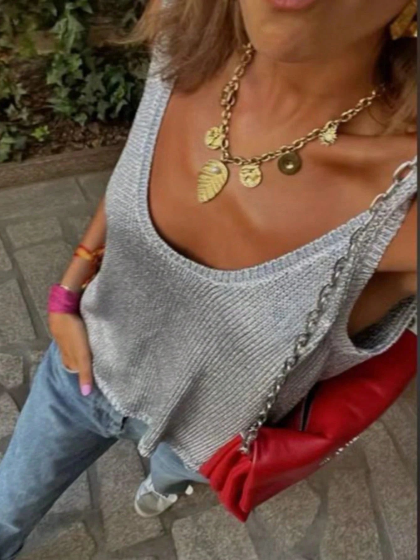 Woman wearing a gray sleeveless top with a red bag, gold necklace, and pink bracelet.