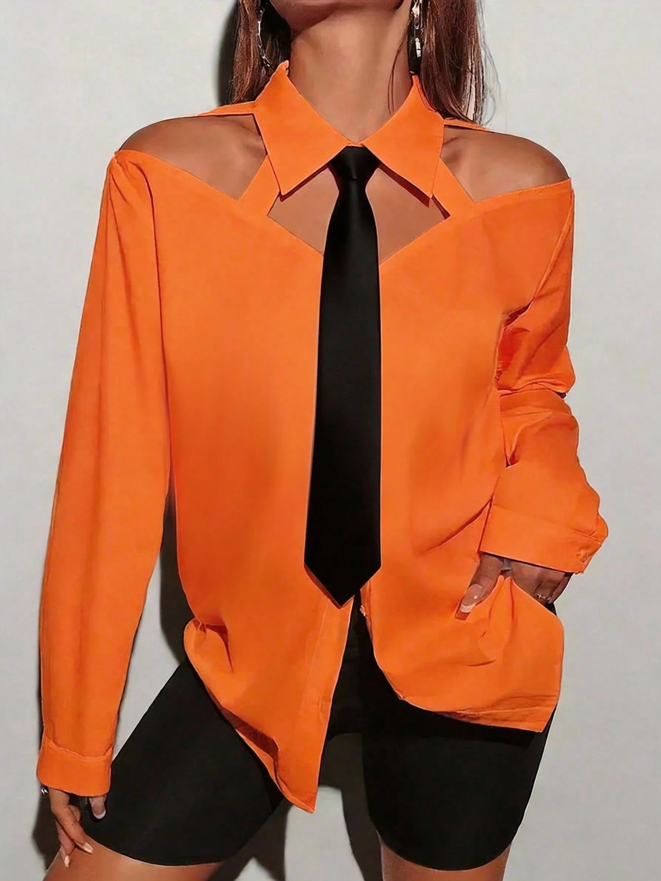 Person wearing an orange shirt with cut-out shoulders against a plain background