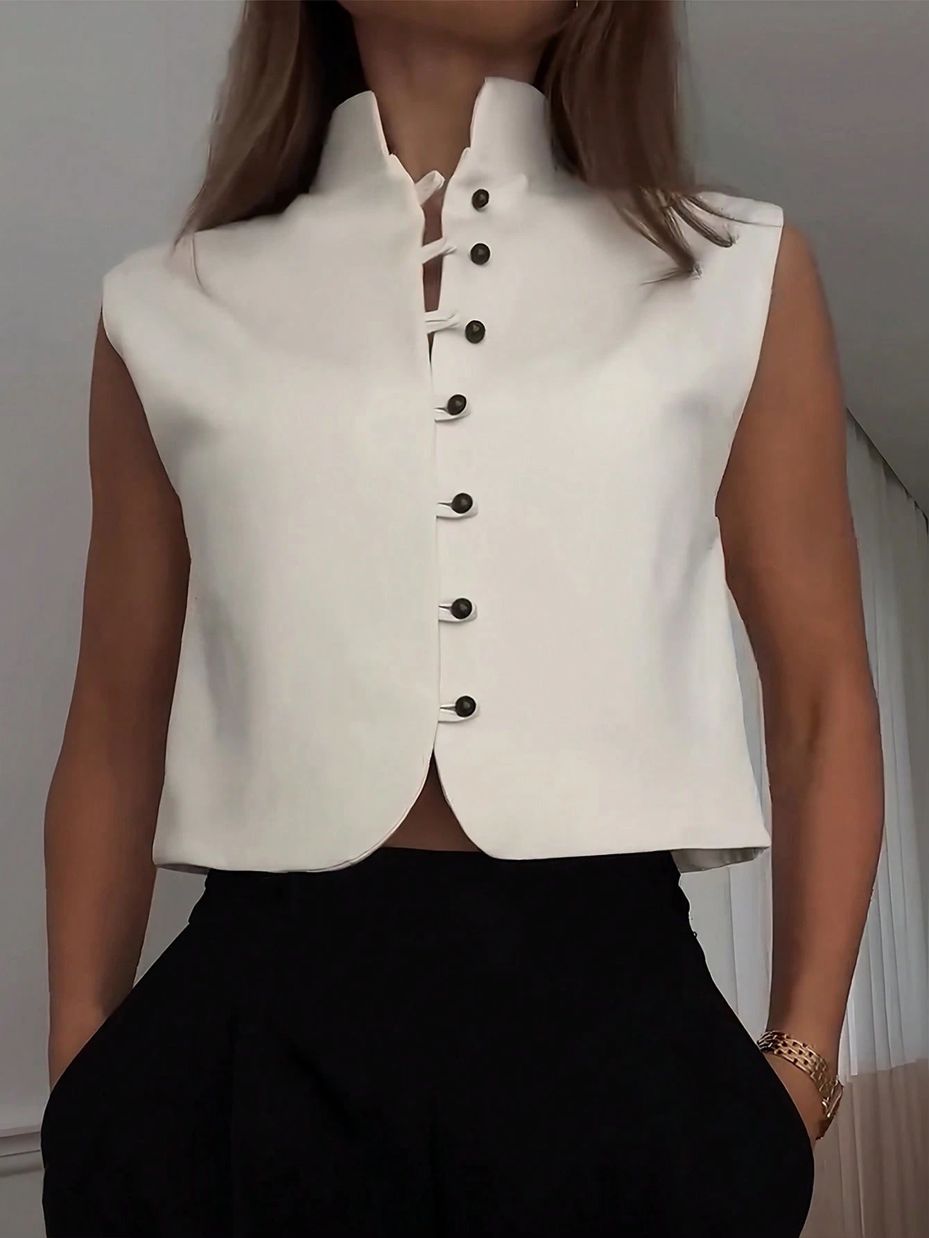 White sleeveless top with black buttons worn by a person against a neutral background