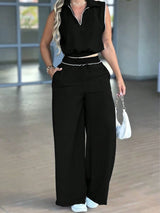 Person wearing a black sleeveless top and wide-leg pants in an indoor setting.