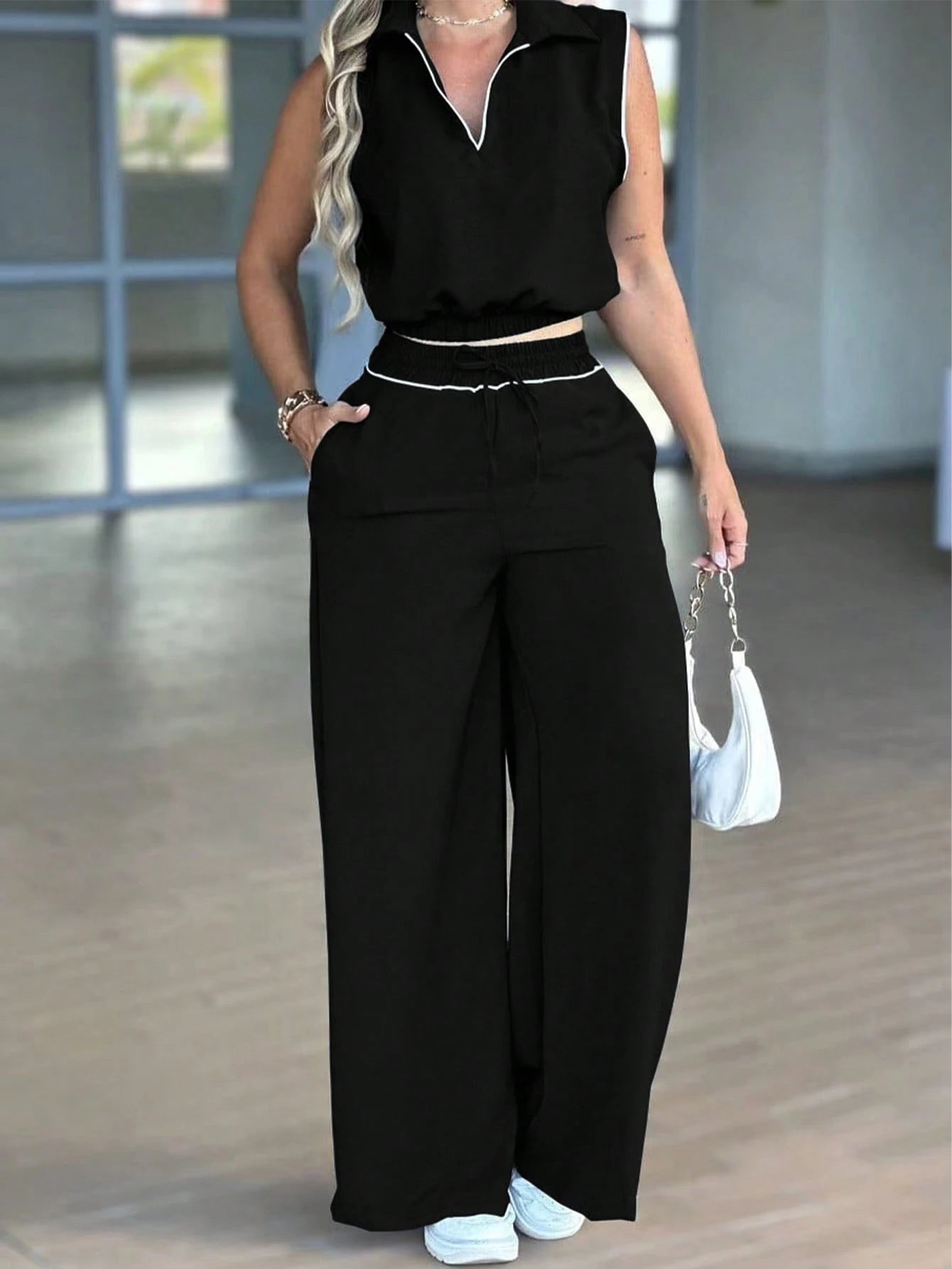 Person wearing a black sleeveless top and wide-leg pants in an indoor setting.