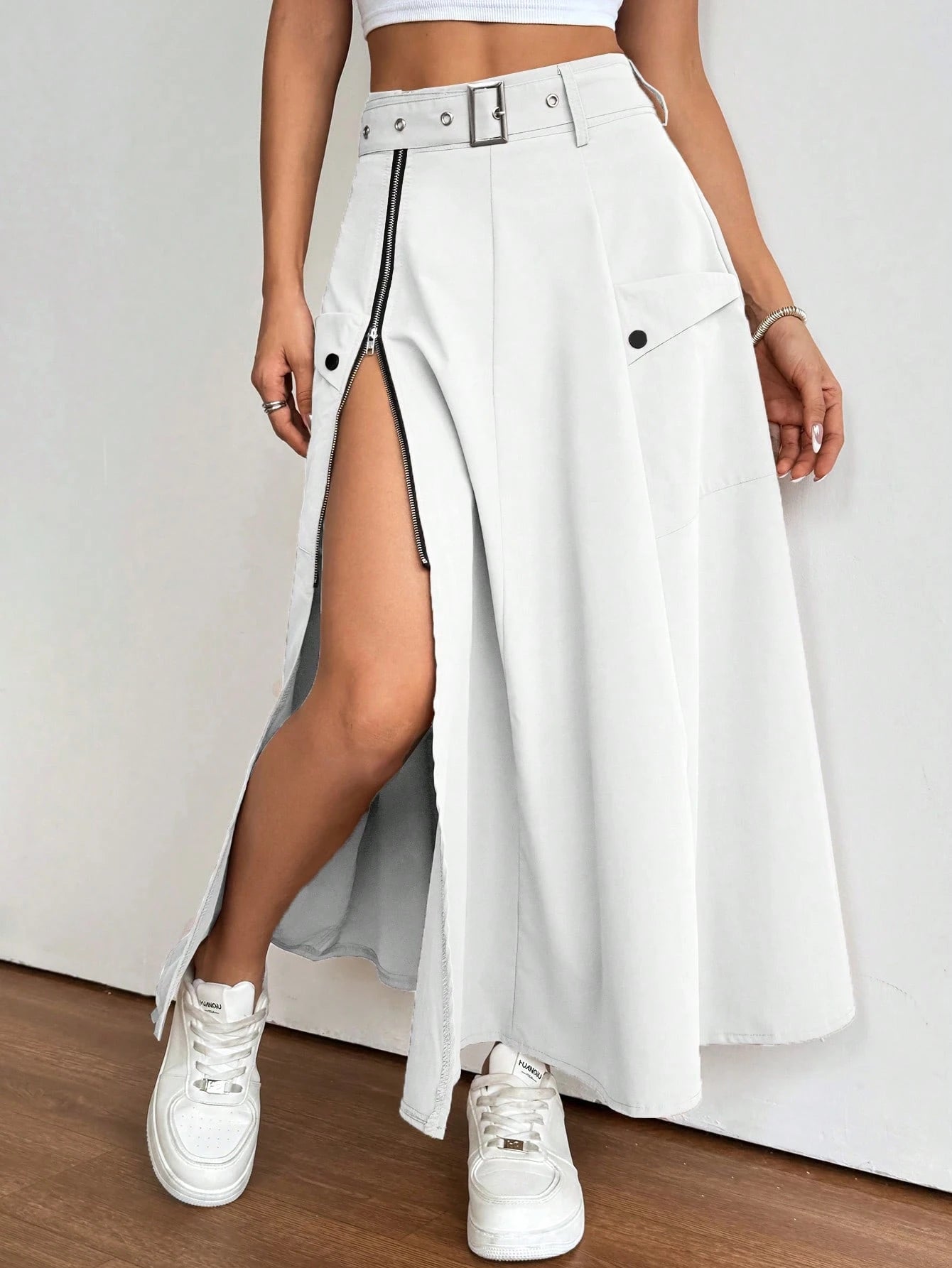 Person wearing a white skirt with a high slit and white sneakers on a plain background
