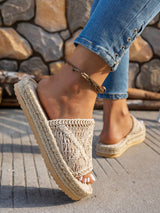 Close-up of a foot wearing a beige wedge sandal with a textured sole, standing on a stone surface.