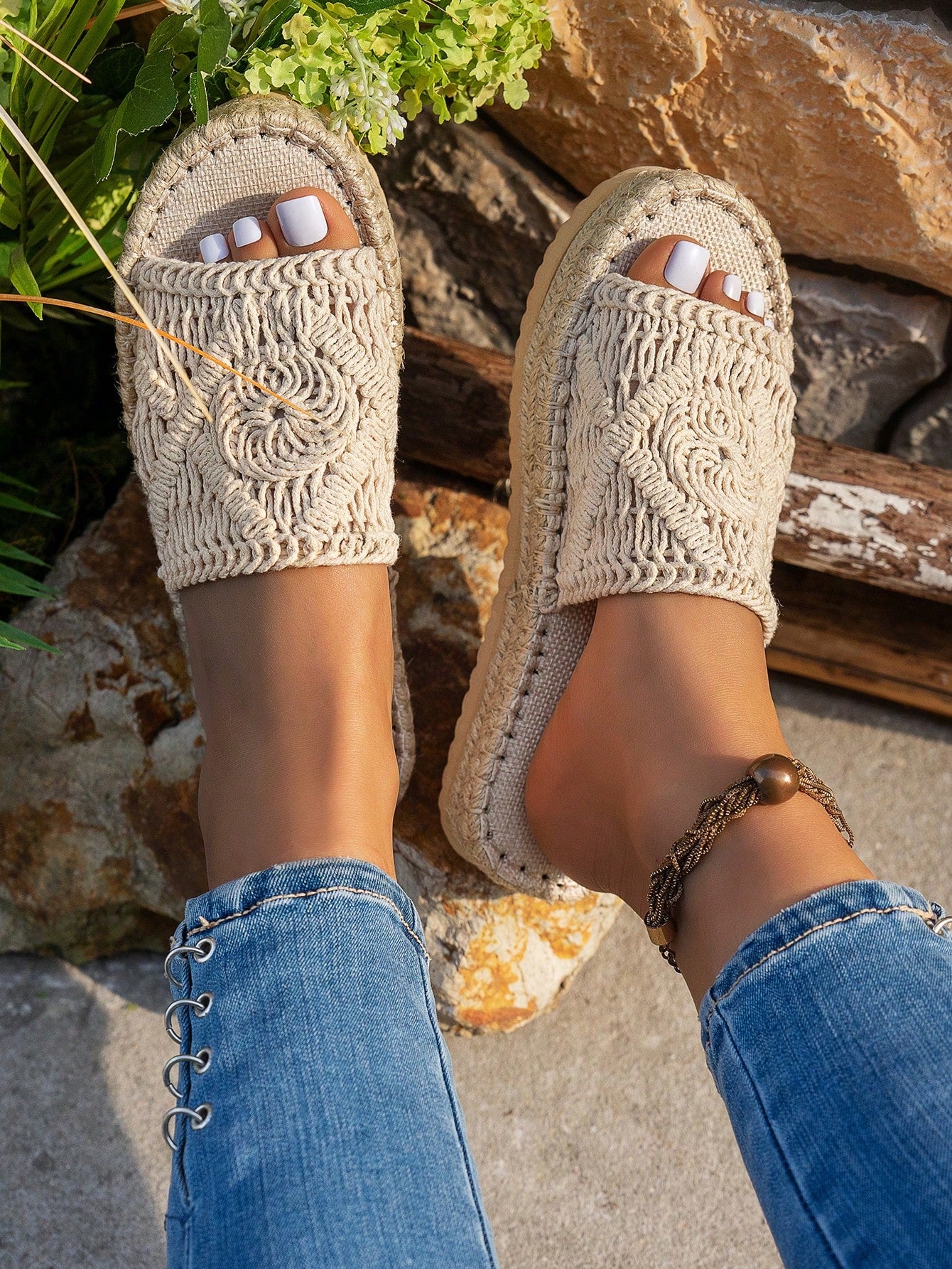 Beige crochet sandals worn with blue jeans against a natural stone background