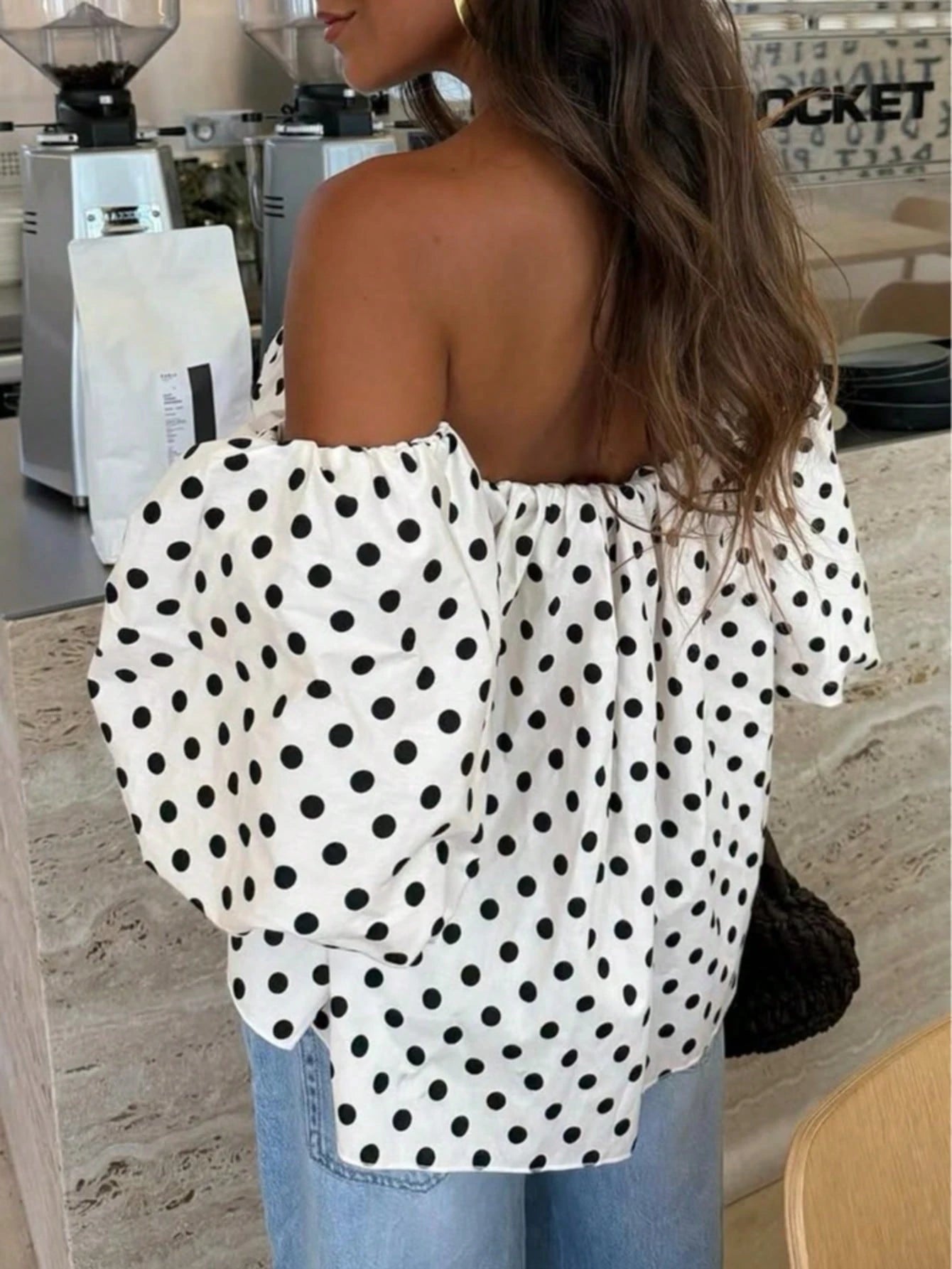 Woman wearing a polka dot off-shoulder top in a cafe setting