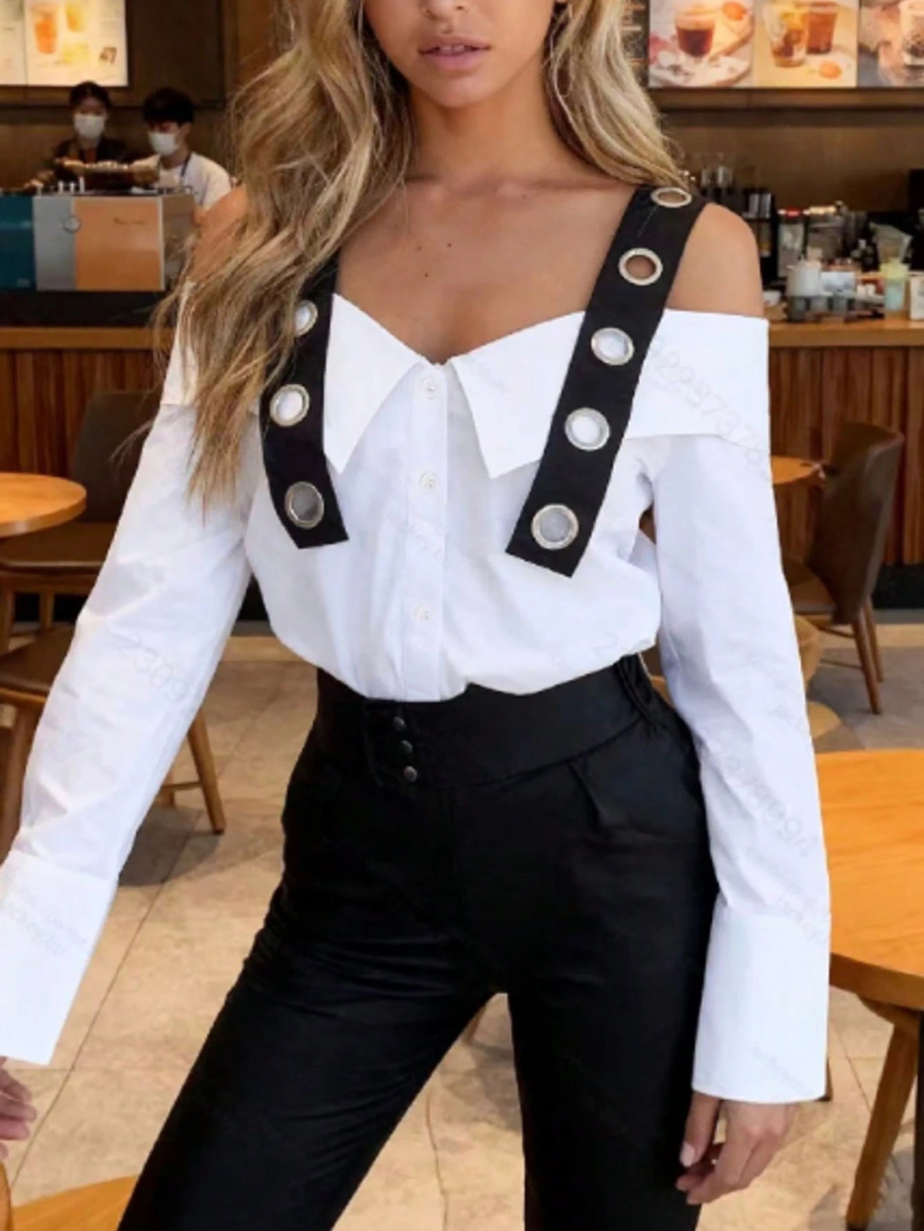 Person wearing a white off-shoulder top with black straps and buttons in a cafe setting