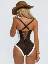 Woman wearing a brown and white swimsuit with a wide-brimmed hat on a light gray background